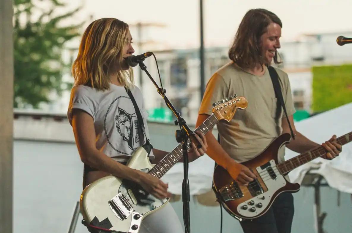 Gitazystka wraz z basistą wykonują utwór muzyczny przed publicznością.